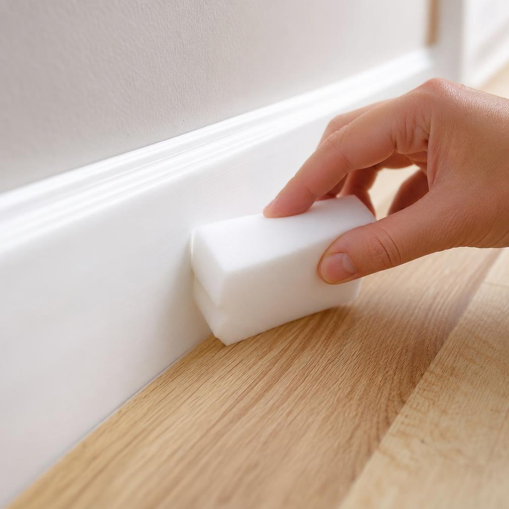 Melamine sponge wiping a white painted baseboard clean