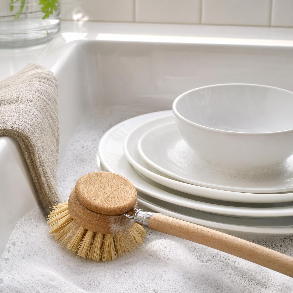 Wooden dish brush beside clean white dishes in a farmhouse sink